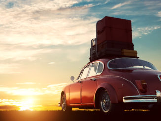 une ancienne voiture rouge, avec des bagages sur le toit face à un coucher de soleil